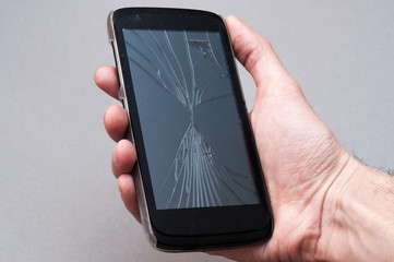 Smartphone with broken screen in hand on grey background.