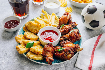 Table fof tasty snacks for beer prepared for watching sports on TV. Chicken. Chicken wings, chicken nuggets, french fries, chips, various sauces and lemonade. Light gray background. Selective focus