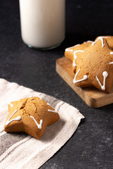 Handmade custard gingerbread in the shape of a star on a black background. Homemade baking. A bottle of milk in the background. Wooden plank. Linen napkin.