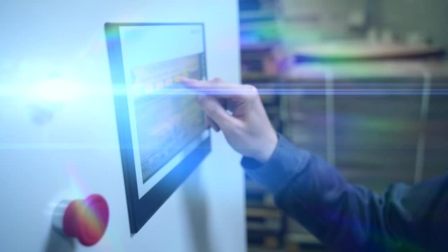 Worker hand clicks touch screen of control panel on industrial computerized equipment of beverage plant or factory in lamp light flare
