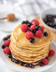 Sweet homemade pancakes with raspberries and blueberries on white plate.
