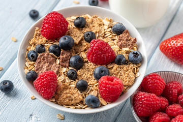 Healthy breakfast of granola chips with blueberries and raspberries on white desk.