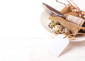 Easter background. Table setting for the holiday of Easter in a rustic style,burlap napkin, quail eggs, fork and knife on a white plate, willow twigs. Copy space, close up