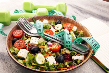 Authentic fresh salad in a stone cup with dumbbells excercise equipment, measuring tape on table. healthy lifestyles, good health Concept with fresh ingredients