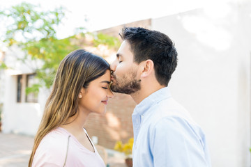 Fototapeta premium Man Kissing Forehead Of Girlfriend Outside Cafe