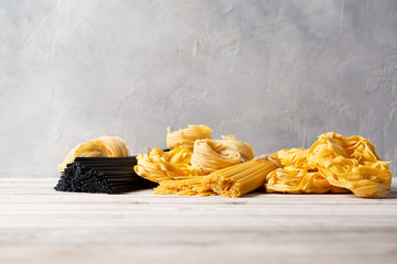 Variety of types and shapes of Italian fresh dry pasta on wooden table. Space for text.