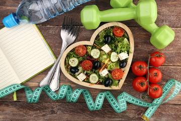 Authentic fresh salad in a wooden heart shaped cup with dumbbells excercise equipment, measuring...