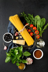 Raw ingredients for cooking spaghetti on a black background. Pasta, tomatoes, garlic, basel, parmesan and olives.