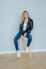 Blonde woman in leather jacket near grey wall. Minimalistic apartment.