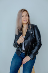 Blonde woman in leather jacket near grey wall. Minimalistic apartment.