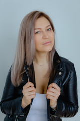 Blonde woman in leather jacket near grey wall. Minimalistic apartment.
