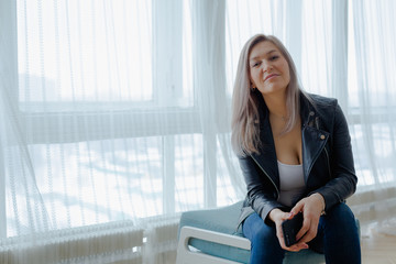 A blonde woman in a black leather jacket in minimalistic appartment.