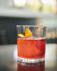 Red alcoholic beverage drink with a sphere ice red cherry and orange zest for decoration