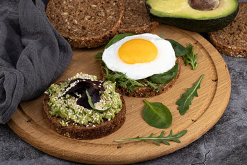 Avocado sandwich on dark rye bread with spinach and fried egg on a dark background
