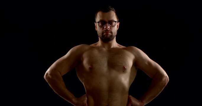 Close-up portrait of a dark-haired man with glasses, he is in the Studio on a black background. His torso is bare, and he straightens as much as possible, pulling his shoulders back.