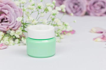 Fototapeta na wymiar Green cosmetic jar with cleansing balm (oil) on a white background with flowers roses and petals, mockup, beauty product and spa concept