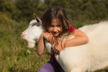 Close Up Of Little Baby Girl Hugs Goat On Meadow In Summer.
