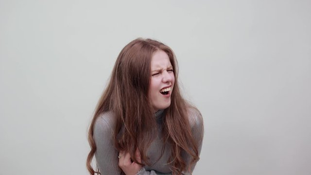 A young beautiful red haired woman in grey sweater is laughing hard leaning in front of very funny