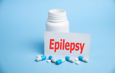 The word epilepsy is written on a card on a blue background, with medical pills and a bottle