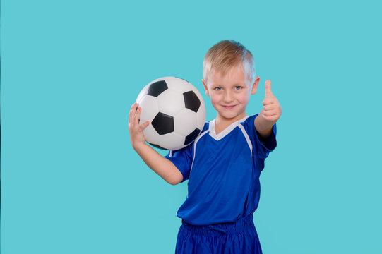 Happy little kid in sportswear holding a soccer ball isolated on blue background