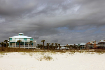 Fototapeta na wymiar Travel America and visit Alabama background.Cloudy seascape with freshly built after hurricane colorful houses for vacation rentals and white sand in a foreground. Alabama Gulf Shores beach area, USA.