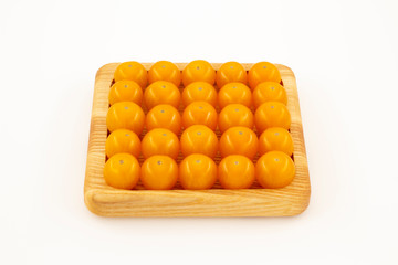 Yellow cherry tomatoes in a wooden rectangular plate on a white background close-up