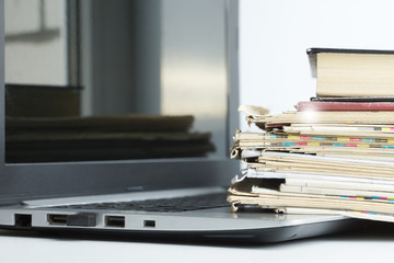 Open Laptop with Books and Newspapers Stacked on its Keyboard in front of Window. News and Information on Paper Pages or Computer Screen, Business Concept