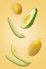 Falling green pickled olives and avocado isolated on yellow background.