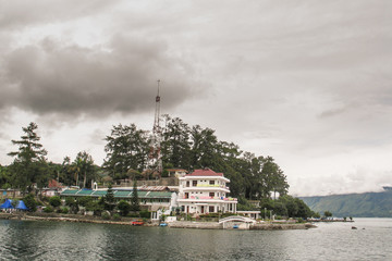 Fototapeta na wymiar Volcanic Island of Samosir on the lake of Toba, on northern Sumatra, Visible typical houses and christian church on the island on a cloudy day.