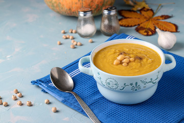 Vegetarian autumn pumpkin cream soup with chickpeas on light blue background, Closeup