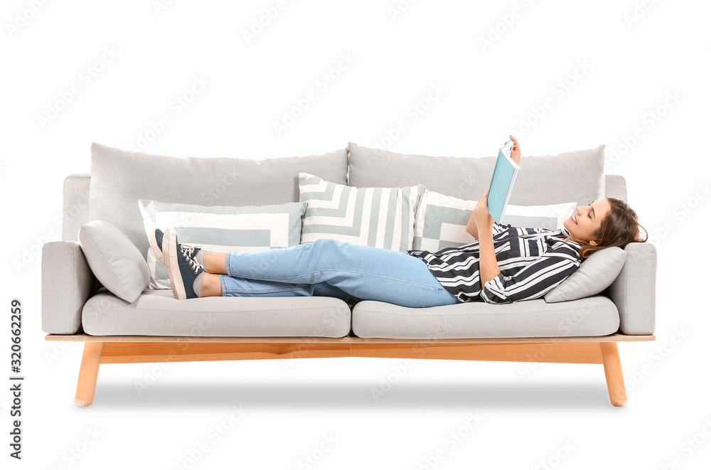 Wall mural young woman reading book while lying on sofa against white background