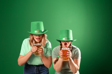 Funny young women with beer on color background. St. Patrick's Day celebration