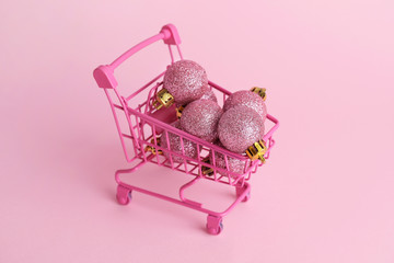 Shopping cart with Christmas balls on pink background