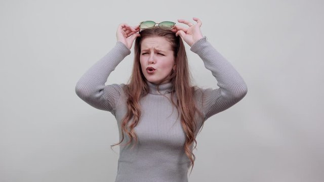a young beautiful red haired woman in gray sweater with goofy smisnim expression funny emotions compressed her lips into tube sunglasses on face