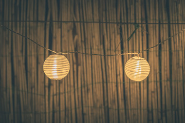 Two round paper lanterns in a home garden on a wooden thatched background at night. Festive decoration in the garden on an evening.