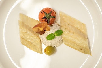 Fancy food on a plate. Slow food dinner menu consisting of fish, olive, prosciutto, parsley, cheese, tomato,...