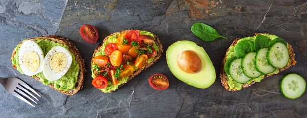 Healthy avocado toasts with eggs, tomatoes and cucumber spinach. Banner orientation flat lay over a...