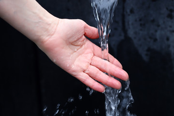 Naklejka na ściany i meble Selective focus. Female hand under a stream of clear water. Splashing water. Cold water source. Drinking water concept.