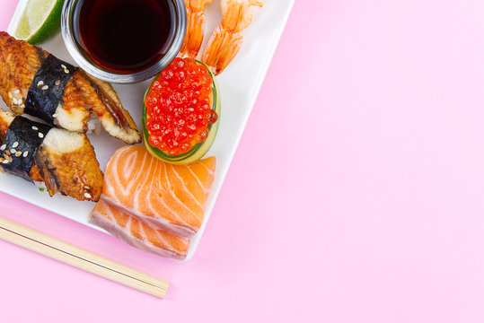 traditional japanese sushi set on a white plate isolated on a pink background. tasty set of sushi, nigiri, sahimi and maki. delicious dinner or lunch for one person. flat lay