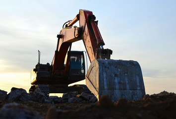 Excavator with a large iron bucket breaks asphalt on a construction site. Demolition work concrete,...