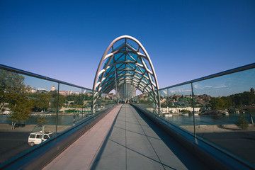 View on the futuristic Bridge of Peace made of glass and metal over a Mtkvari river in the center of old Tbilisi. Sunny weather. Outdoor shot