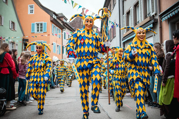 Bajass aus Waldkirch - große Gruppe Narren in gelb-blauem Gewand mit Anführer in der Mitte, bei Fastnachtumzug in Staufen, Süd-Deutschland