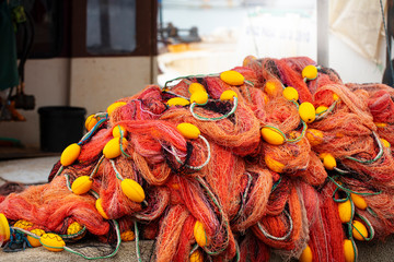 Fishing net of orange and yellow ropes and stack of buoys on the dock.