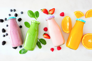 Assorted healthy smoothies in bottles with ingredients. Top view flat lay against a white marble...