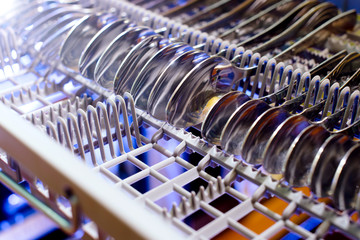 An open dishwasher with clean flatware, front view. selective focus on spoons and forks, closeup