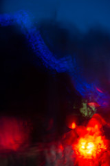Fototapeta premium abstract bokeh caused by rain drops reflecting onto car windscreen from car brake lights and city street bridge lights on dusk. Indistict focus applied.