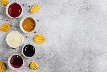White bowls of various dip sauces on gray background. Mustard, ketchup, cheese, teriyaki and cranberries sauces. Top view with copy space. Flat lay