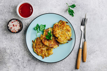 Homemade potato pancakes or hash brown on blue plate with sauce on gray table. Traditional dish in European and American cuisine. Top view.
