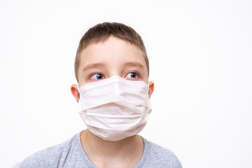 A caucasian boy in white face surgical mask on white background, protection against flu and virus infection