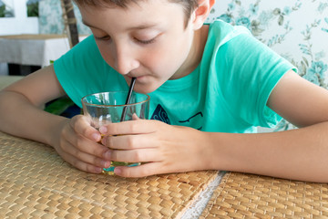 A thirsty preteen boy drinking juice through a straw from a glass in a restaurant